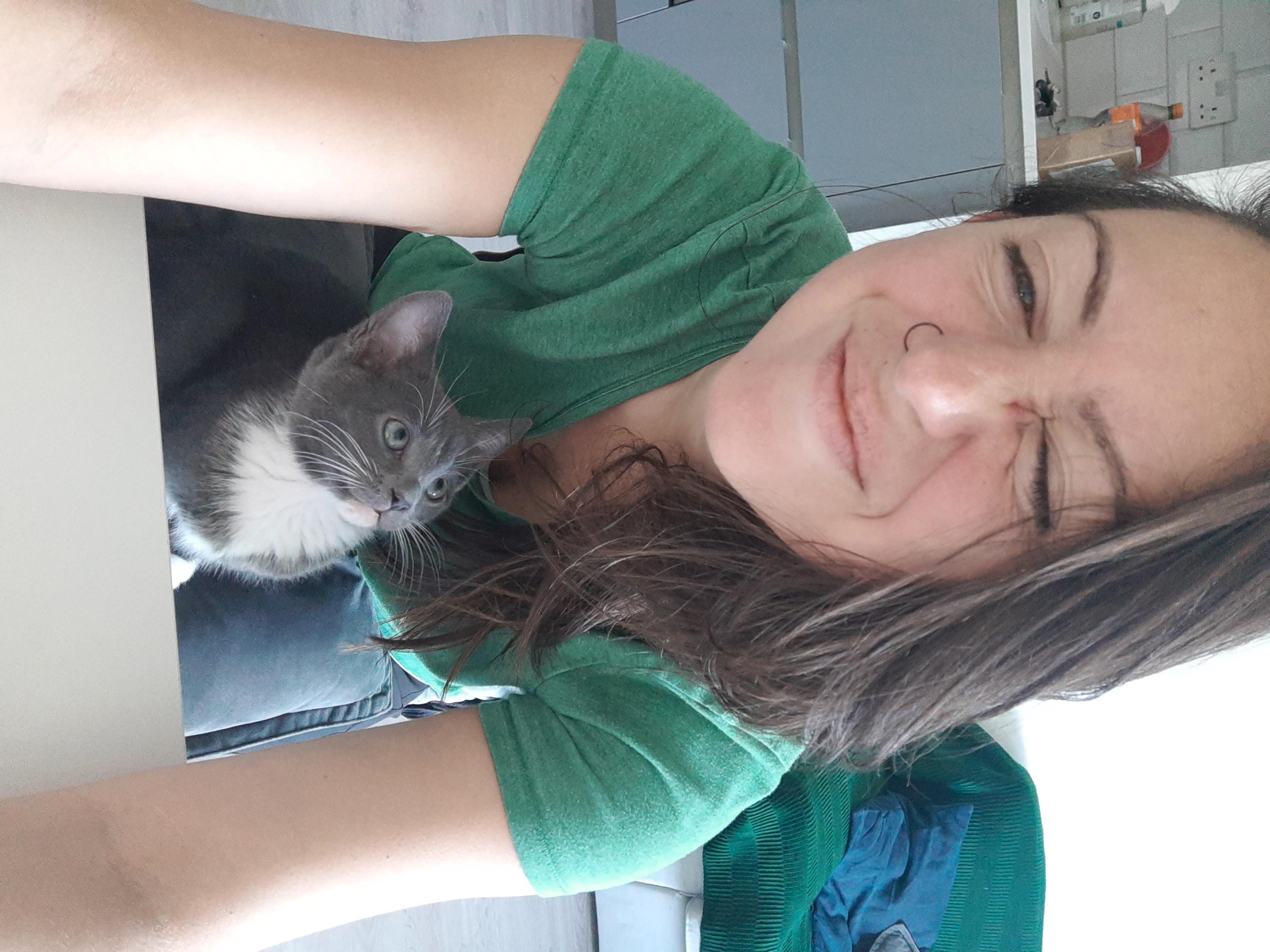 Sam in a green top sitting on a sofa with a grey and white cat resting beside her